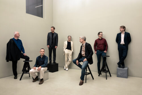 Zu sehen sind die Mitglieder des Ensembles Ascolta. Teilweise sitzen oder stehen sie auf Barhockern oder Kisten.