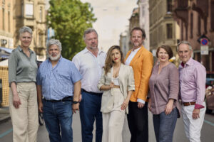 Zu sehen sind die sieben Sänger:innen der Neuen Vocalsolisten. Sie posieren in einer Reihe. Im Hintergrund sind die Fassaden der Stuttgarter Tübingerstraße zu sehen.