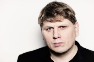 Das Porträt eines Mannes (Sergej Newski). Er blickt geradeaus und trägt ein schwarzes Oberteil.