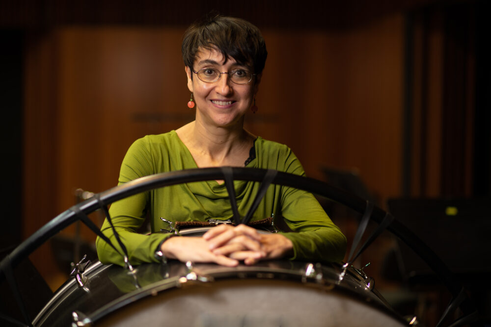 Zu sehen ist ein Portrait der Komponistin Elena Mendoza. Sie steht hinter einer großen Trommel.