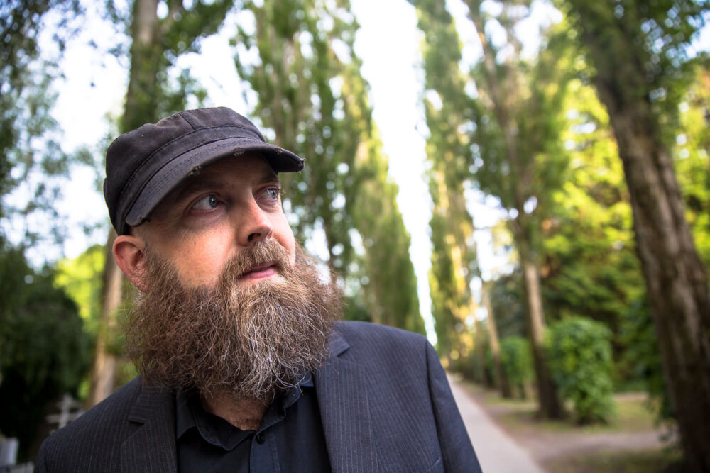 Zu sehen ist der Komponist Christan Winther Christensen. Er steht vor eiener langen Baumallee.
