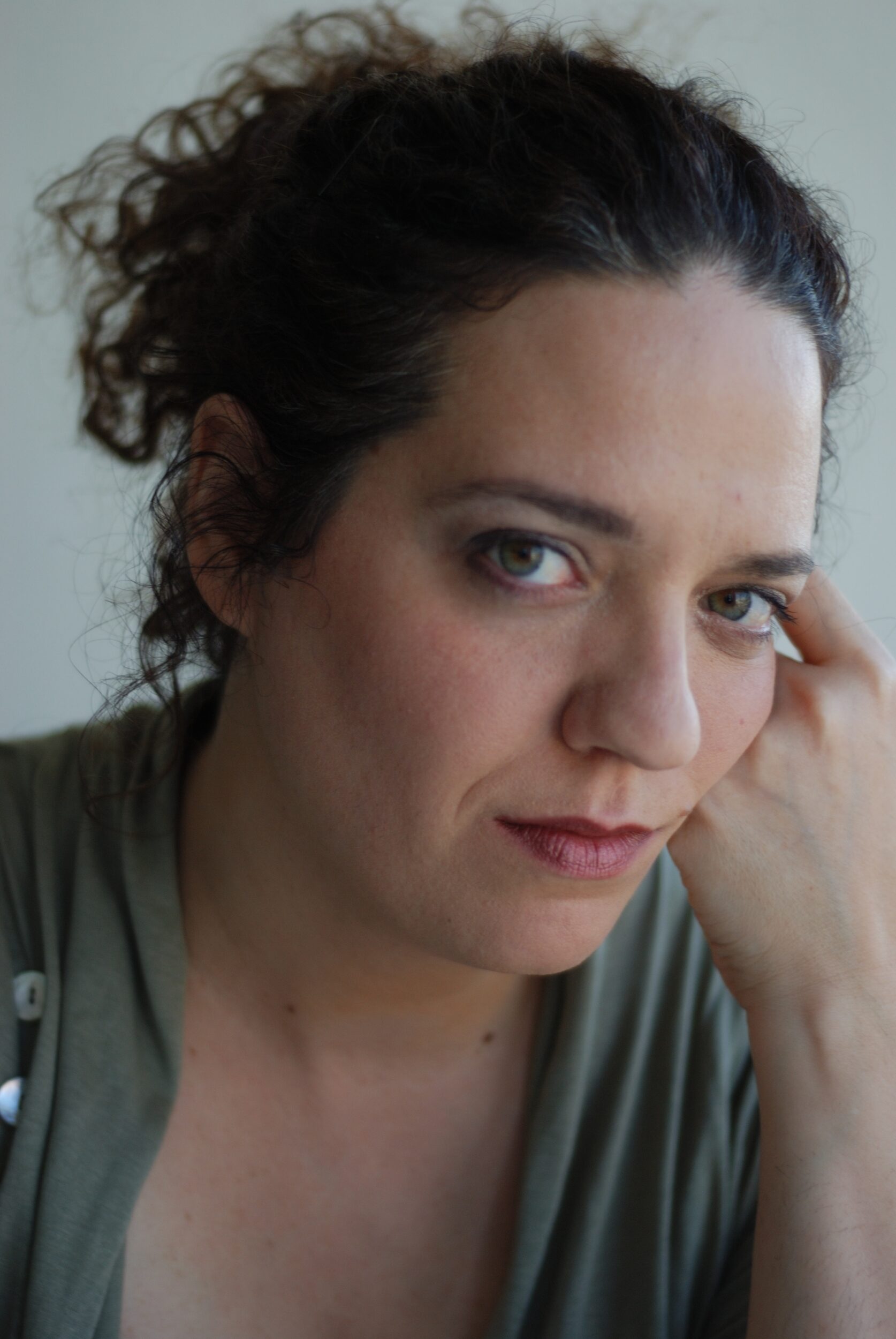 Zu sehen ist ein Portrait von Noa Frenkel. Sie stützt ihren Kopf auf ihrem linken Arm ab und blickt entspannt in die Kamera. Sie trägt ein grünes Oberteil.