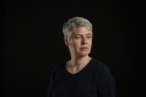 Das Bild zeigt ein Porträt der Mezzosopraistin Truike van der Poel. Sie ist zu sehen mit kurzem, grauem Haar vor einem schwarzen Hintergrund. Sie trägt ein schwarzes Oberteil und blickt zur Seite.